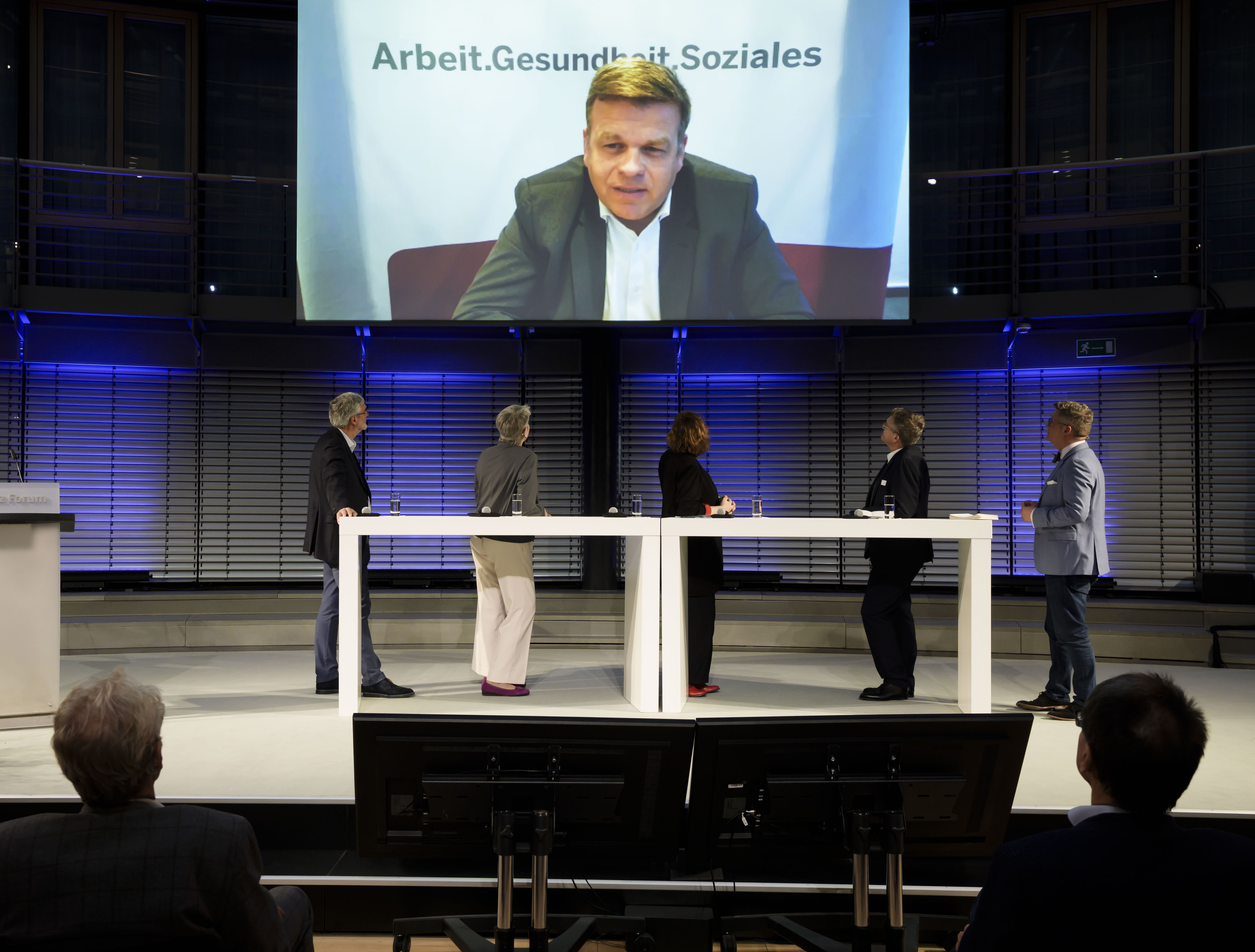 Podiumsdiskussion bei Ausgezeichnete Gesundheit mit digital zugeschaltetem Referenten auf Großbildschirm