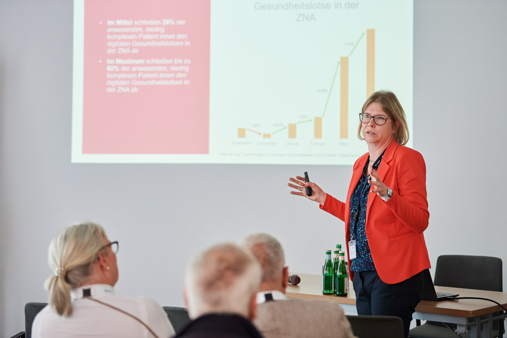 Eine Frau hält einen Vortrag, im Hintergrund ist die Präsentation an die Wand projiziert.