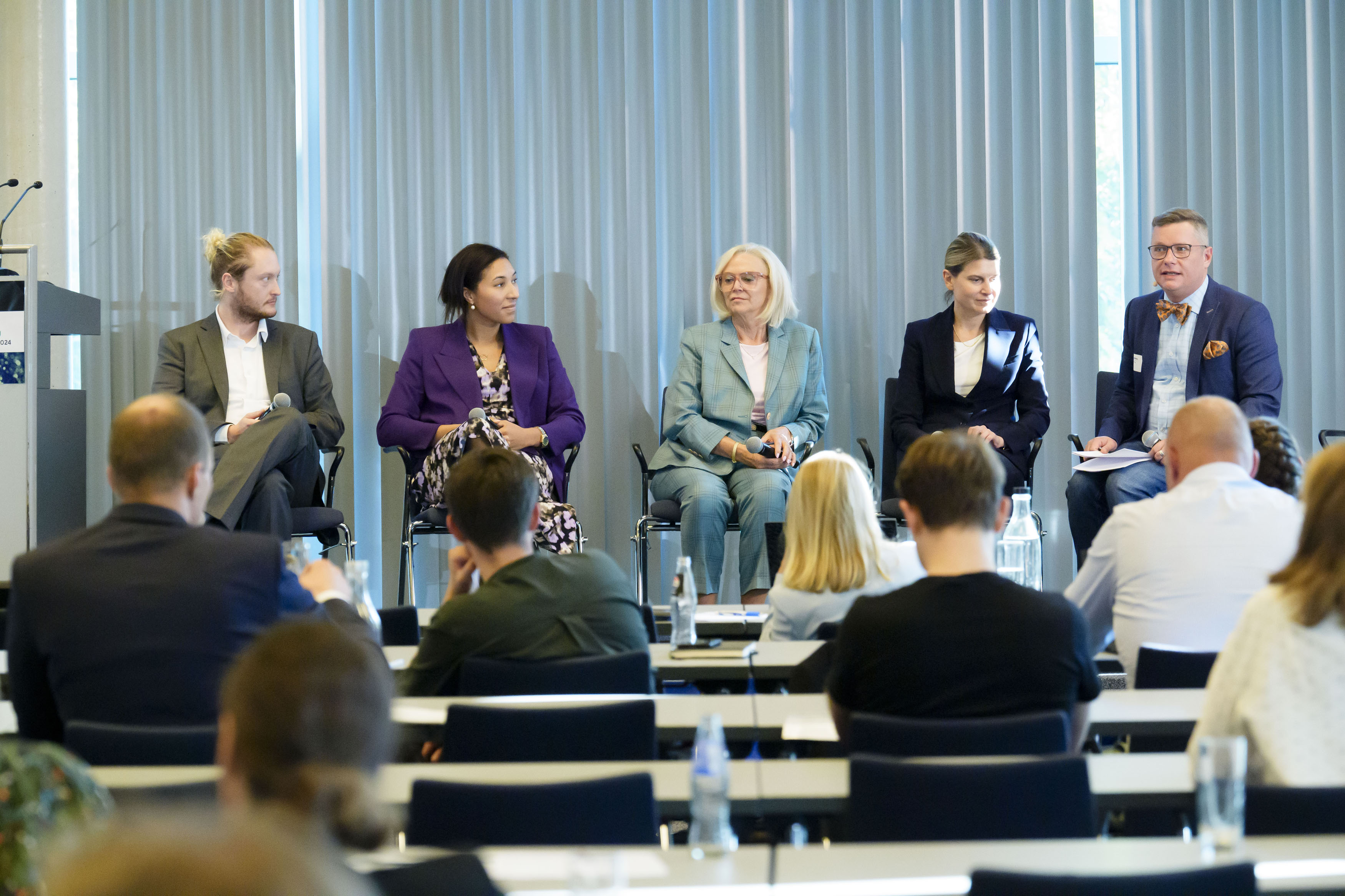 Podiumsdiskussion mit 4 Diskutierenden, Moderator und Publikum