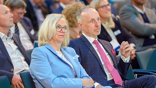 Dr. Annette Rommel und Dr. Stephan Hofmeister hören in der ersten Reihe des Publikums den Vorträgen zu.