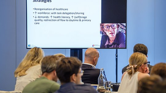 Leinwand mit Folienpräsentation und Video der digital zugeschalteten Vortragenden