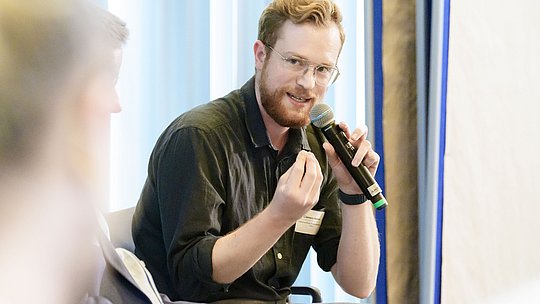 Podiumsteilnehmer mit Handmikrofon während seines Wortbeitrags