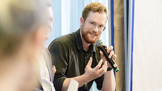 Podiumsteilnehmer mit Handmikrofon während seines Wortbeitrags