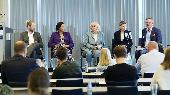 Podiumsdiskussion mit 4 Diskutierenden, Moderator und Publikum
