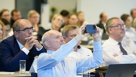 Publikumsgast fotografiert Vortragsfolien mit seinem Handy