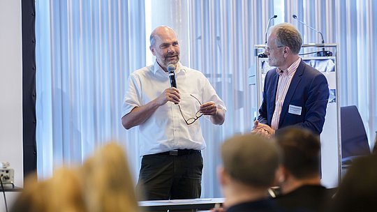 Prof. Dr. Reinhard Busse mit Handmikrofon neben Dr. Dominik von Stillfried